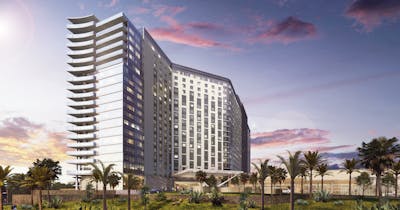 Sunset sky backdrop behind a multi-story modern building featuring angular architecture, abundant windows, and glass-framed balconies. Below, a tropical-themed landscape with palm trees, lush foliage, and a verdant lawn.