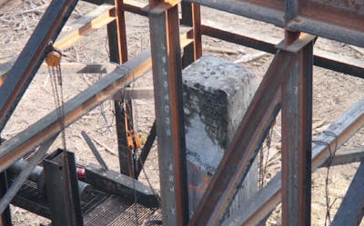 Close up of a concrete pile, surrounded by steel support beams, pullies and cables.