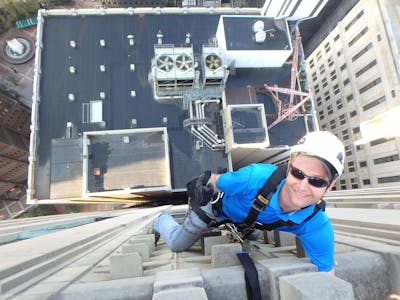The man is climbing up the side of the Koppers Building with ropes.