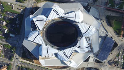 An aerial view of an open-roof stadium, with its roof components arranged to resemble a flower with eight petals.