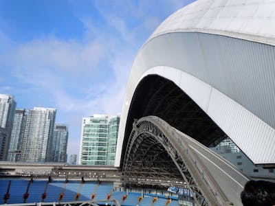 An open-roof stadium with a towering cityscape backdrop against a vibrant blue sky.